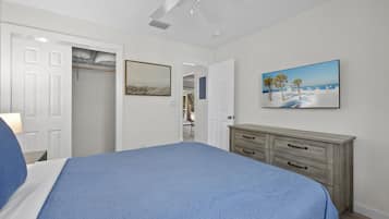 A bedroom with a bed, a dresser, a ceiling fan, a painting, and a closet.