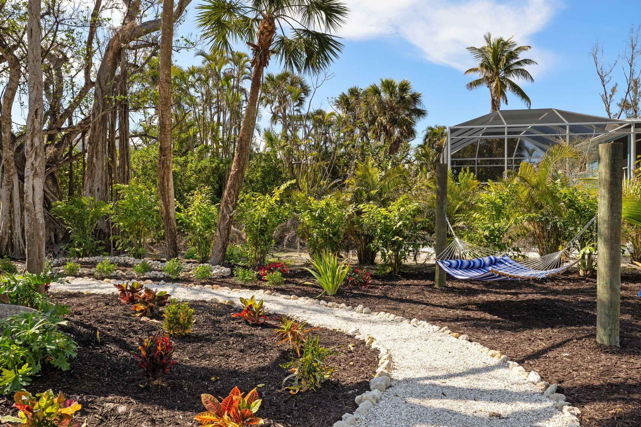 A garden with a hammock, palm trees, and a greenhouse structure.