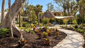 A garden with a thatched-roof structure, palm trees, and a gravel path. - Driftwood Inn (Sanibel)