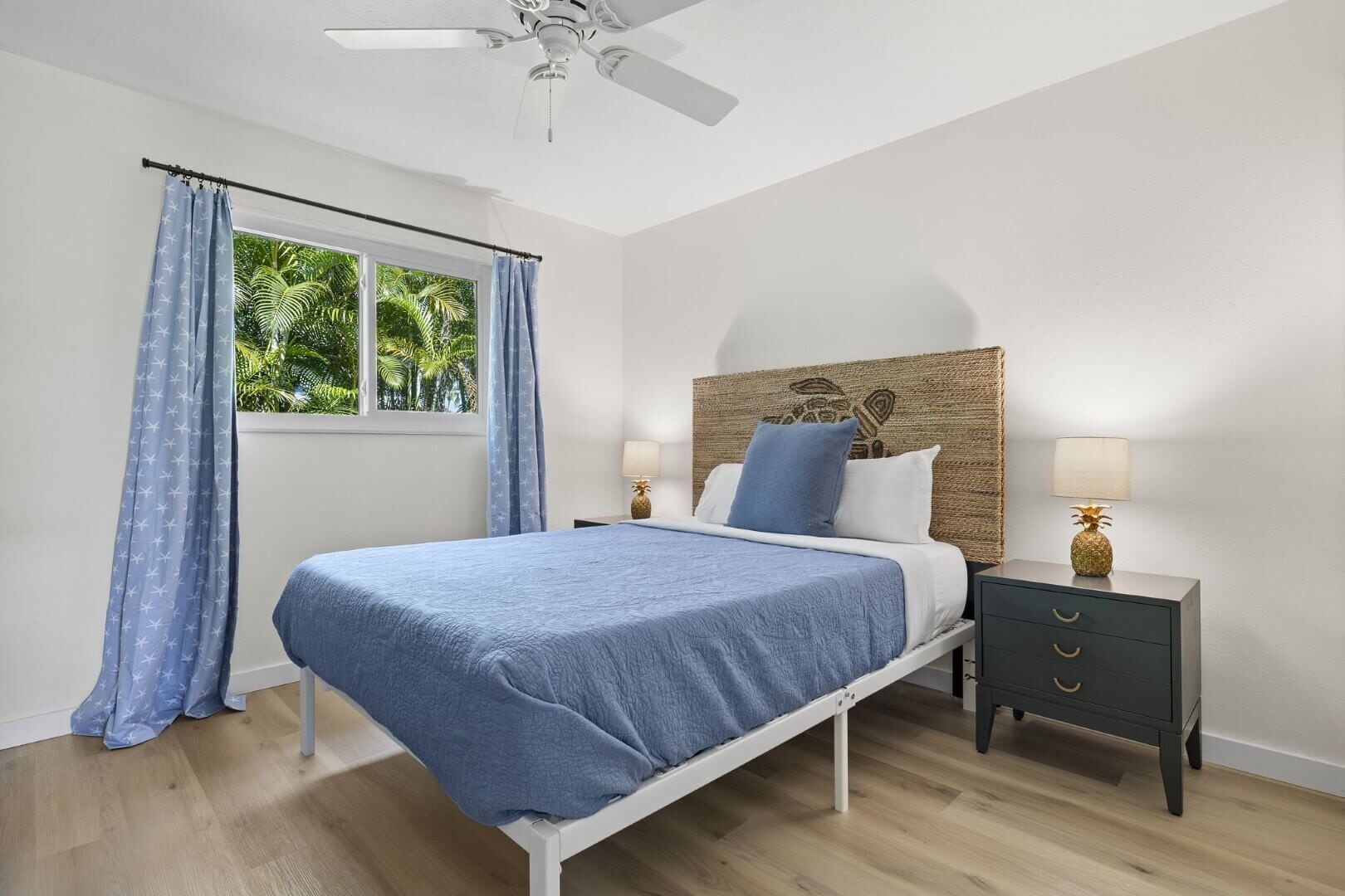Un dormitorio con cama, mesita de noche, ventilador de techo y ventana con cortinas.