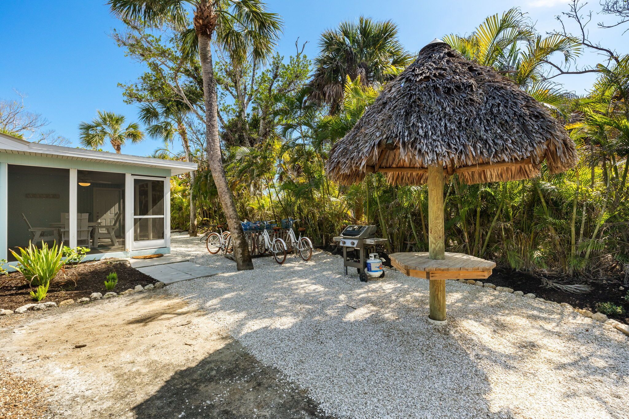 A thatched-roof outdoor area with a grill, bicycles, and a building with a sliding glass door.
