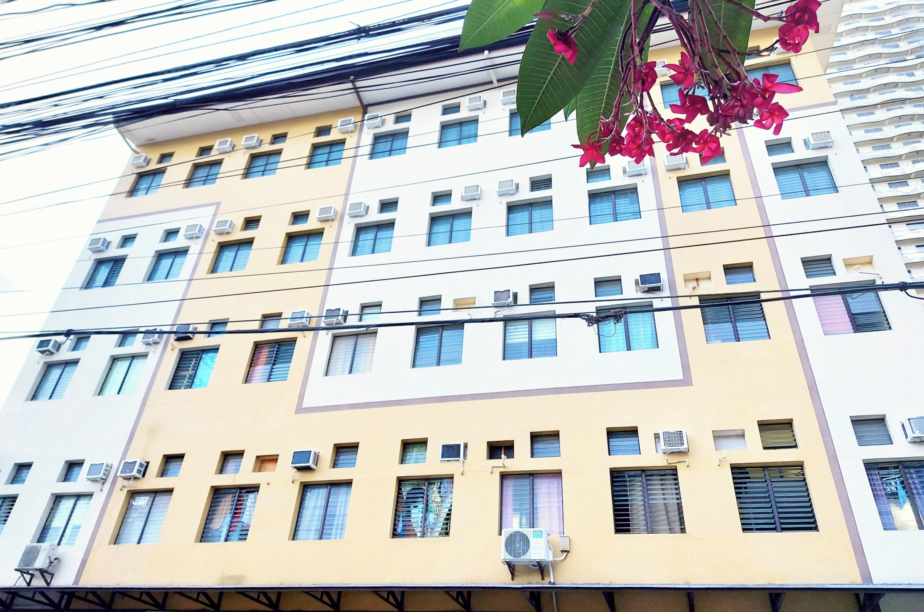 A multi-story building with air conditioning units, windows, and a visible balcony.