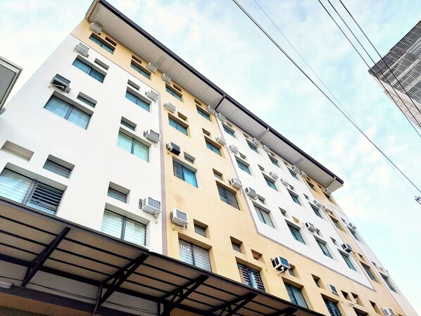 Un edificio de varios pisos con fachada plana, numerosas ventanas y unidades de aire acondicionado.