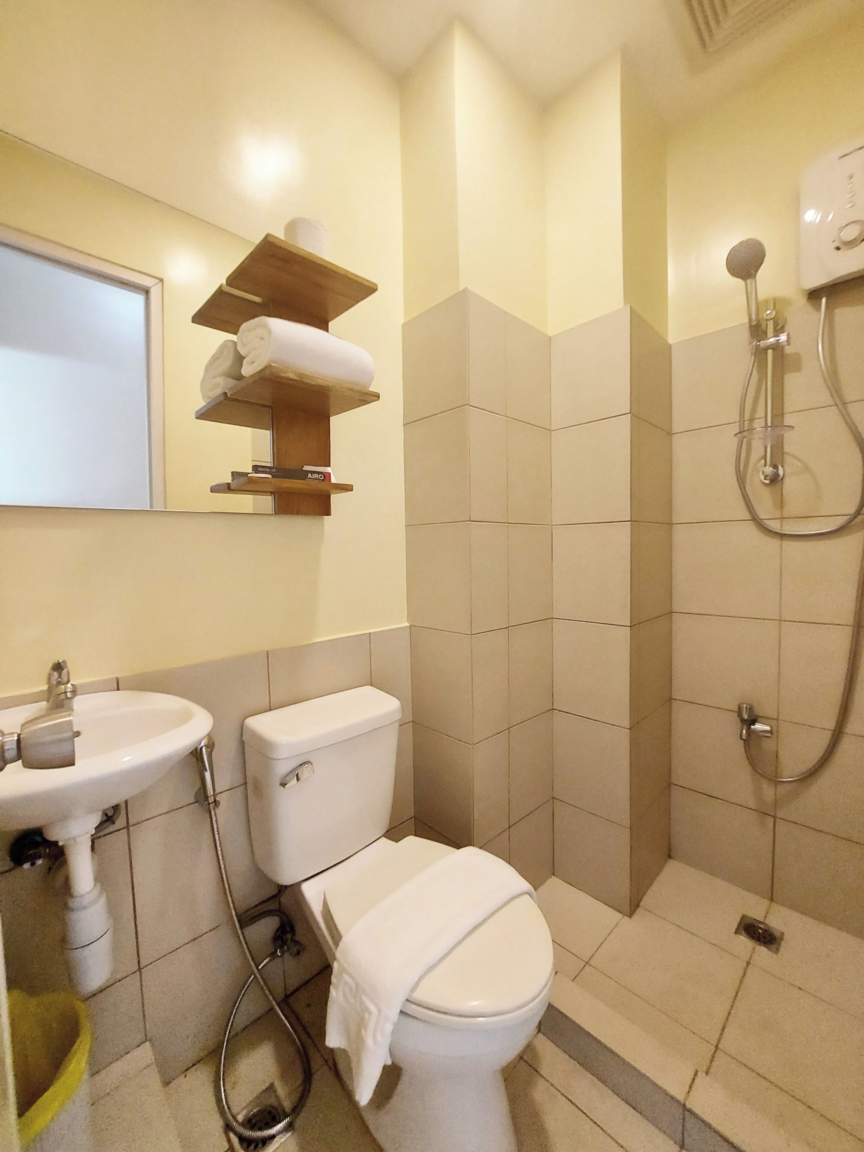 A bathroom with a toilet, sink, and shower. There are towels on a shelf above the sink.