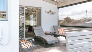 A covered outdoor seating area with wicker lounge chairs and a white bench. - Mara House - Space for Everyone (Break O'Day)