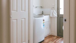A compact kitchen with a refrigerator, a sink, and a towel hanging on the door. - Mara House - Space for Everyone (Break O'Day)