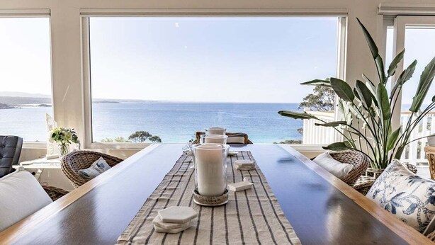 Un comedor con vistas al mar, una mesa con velas y mobiliario de mimbre.