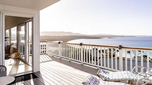 Un balcón con vista al mar, baranda blanca y mobiliario exterior.