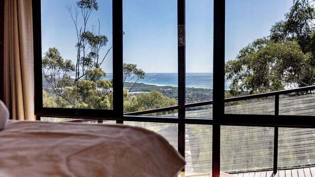 A room with a large window offering a view of the ocean and surrounding trees.