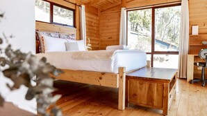 A wooden cabin bedroom with a bed, a desk, and large windows.