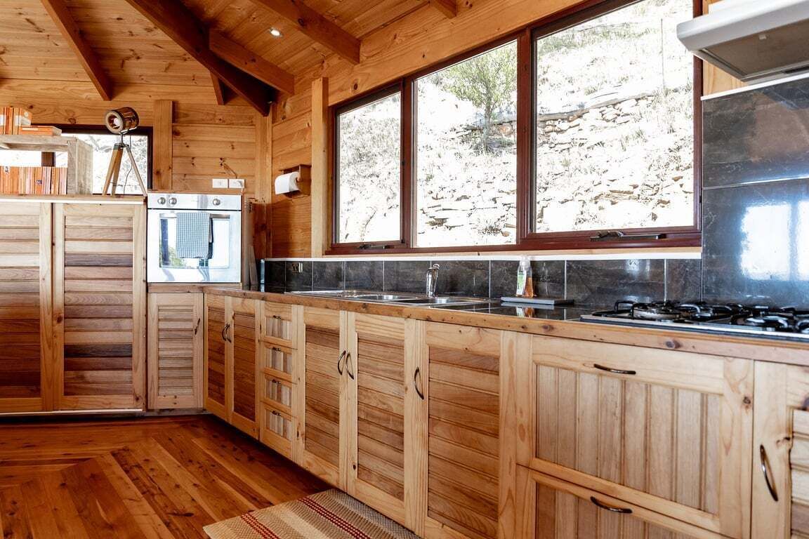 A wooden cabin kitchen with large windows, a stove, and wooden cabinets.