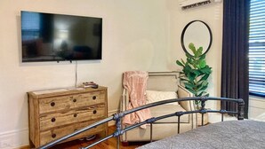 A bedroom with a bed, a wooden dresser, a television, a potted plant, and a window with curtains.