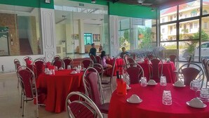 A dining area with red tables and chairs, large windows, and a view of a building outside. - Royal Hotel Cua Lo Beach (Cua Lo)