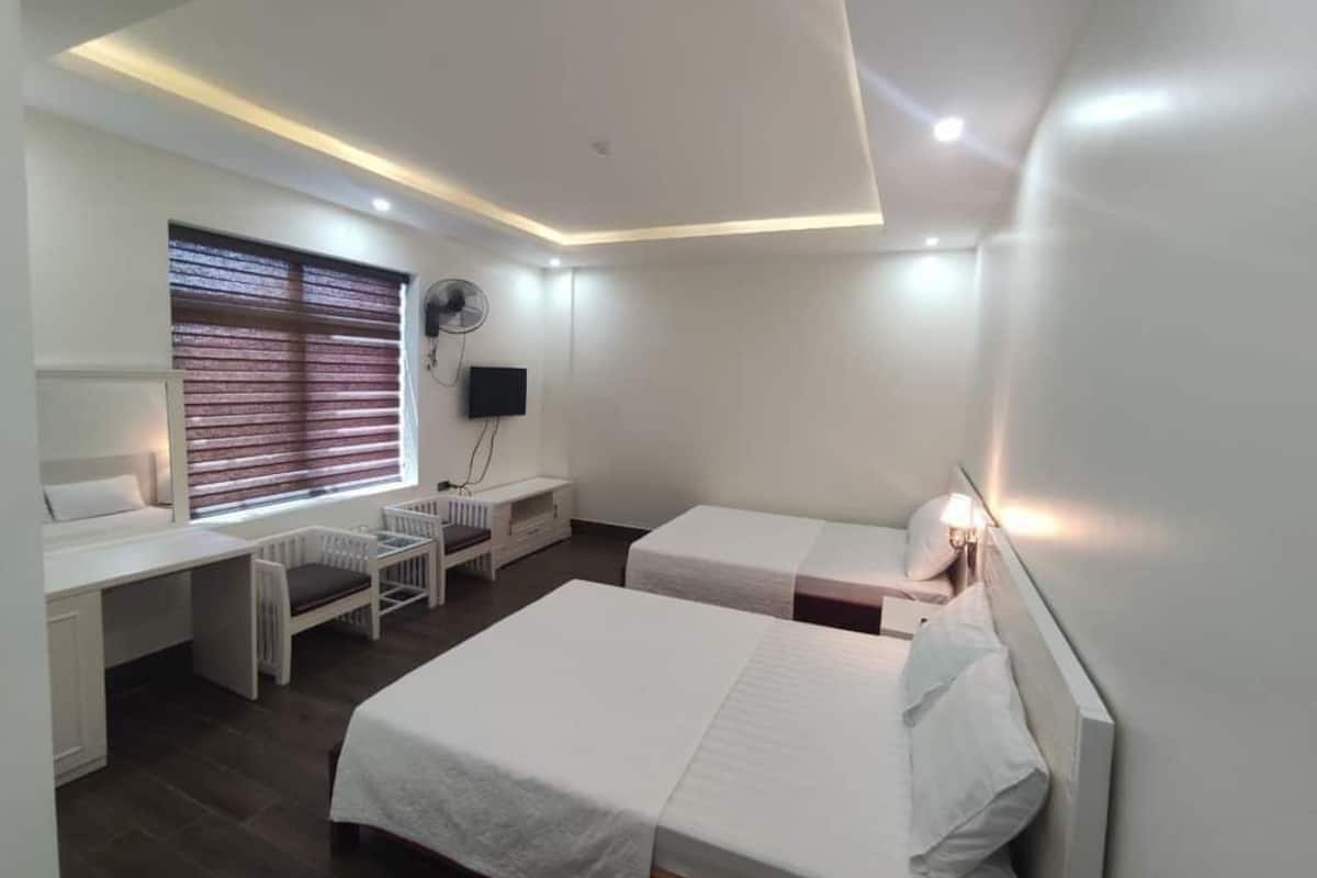 A hotel room with two beds, a desk, a chair, a TV, and a window with blinds.