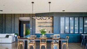 A modern living room with a dining area, featuring a large window with a view, a sofa, and a dining table with chairs. - Riverbank  - Hosted by NZSIR Luxury Rental Homes (Wānaka)