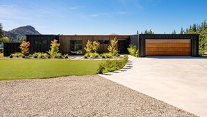 A modern house with a large garage, a well-maintained lawn, and a gravel driveway. - Riverbank  - Hosted by NZSIR Luxury Rental Homes (Wānaka)