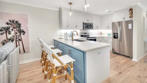 Une cuisine moderne avec des meubles blancs et bleus, des appareils en acier inoxydable et un îlot central doté de tabourets de bar.