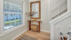 Un couloir avec une console en bois, un panier en osier, un miroir et un escalier.