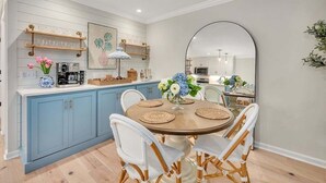 Une cuisine avec des meubles de couleur bleue, une table ronde en bois et quatre chaises, ainsi qu’un grand miroir accroché au mur.