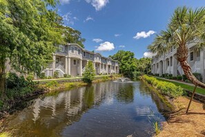 A canal with a fountain, surrounded by trees and a row of buildings with balconies. - Less than a Mile to the Beach! Community Pool. (Saint Simons Island)