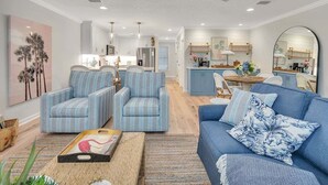 Un salon moderne avec des fauteuils à rayures, un canapé bleu et une cuisine en arrière-plan.