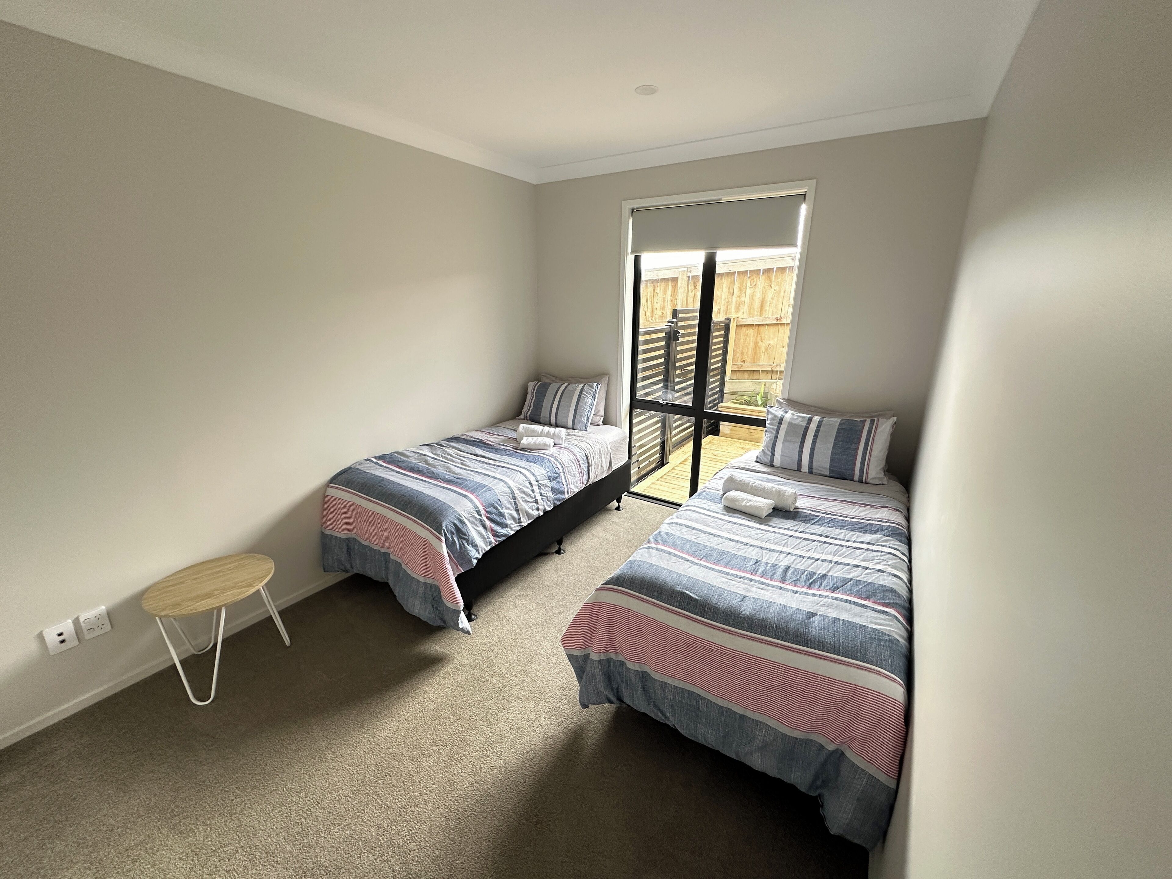 A bedroom with two beds, a small round table, and a sliding glass door leading to an outdoor area.