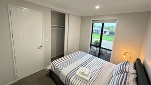 A bedroom with a bed, a closet, a window with a view of a house, and a nightlight.