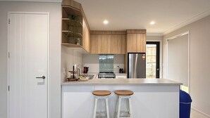 A modern kitchen with white cabinetry, a stainless steel refrigerator, a gas stove, and two wooden stools.