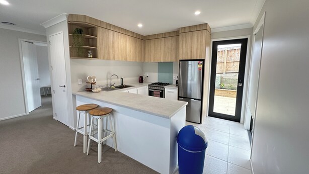A modern kitchen with wooden cabinets, a stainless steel refrigerator, a sink, and two stools.
