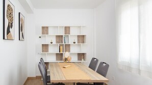 A dining area with a wooden table, four chairs, and a white shelving unit with various items.
