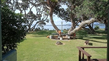 A grassy outdoor area with picnic tables and a bench, overlooking a body of water.