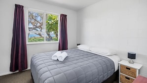 A hotel room with a bed, a nightstand, a lamp, and a window with curtains. - The Sands Motel (Tutukaka)