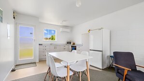 A modern kitchen with white cabinets, a white refrigerator, and a microwave. There is a dining table with four chairs. - The Sands Motel (Tutukaka)