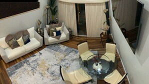 A modern living room with a glass-top coffee table surrounded by four chairs, a white sofa with decorative pillows, and a large abstract rug. - Lake Conroe w/Theatre, Views, & Boat Launch Access & Walden's endless amenities  (Montgomery)