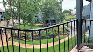 A balcony with a view of a landscaped area including a pond, trees, and buildings. - Lake Conroe w/Theatre, Views, & Boat Launch Access & Walden's endless amenities  (Montgomery)
