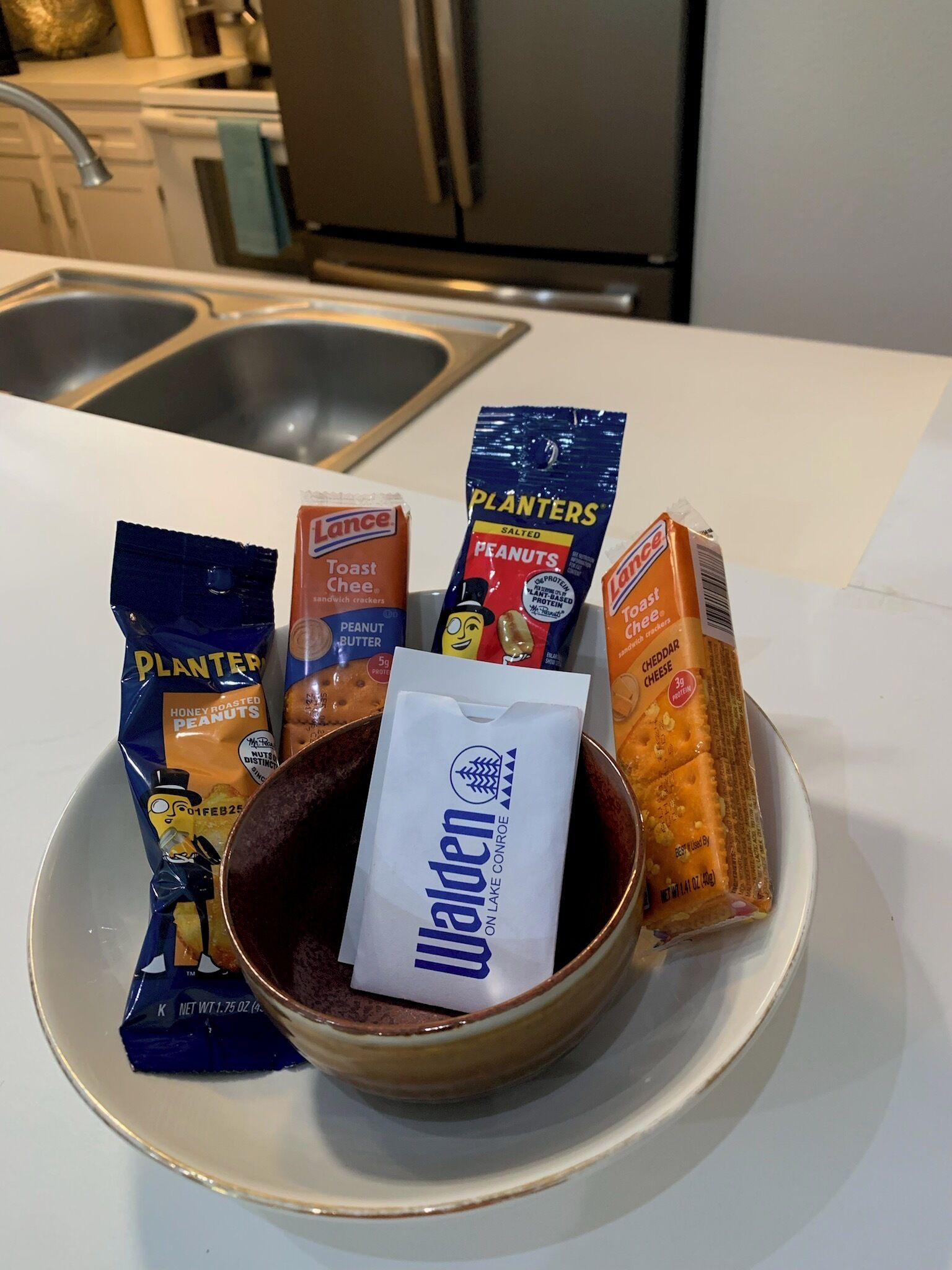 A bowl of snacks on a plate with various packaged snacks around it.