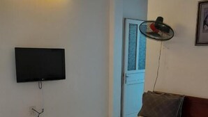 A bedroom with a bed, a television mounted on the wall, and a standing fan.