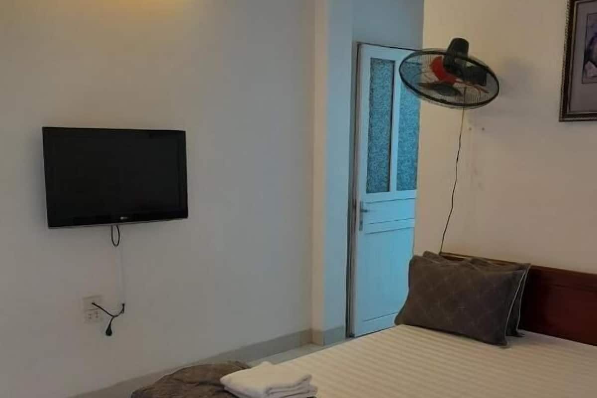 Ein Schlafzimmer mit einem Bett, einem an der Wand befestigten Fernseher und einem Standventilator.