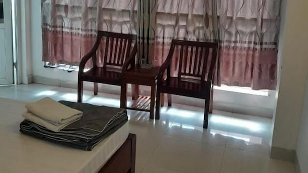A bedroom with a bed, two wooden chairs, and a window with patterned curtains.