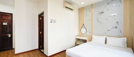 A hotel room with a bed, a wooden floor, a marble wall, a wooden door, and an air conditioning unit.
