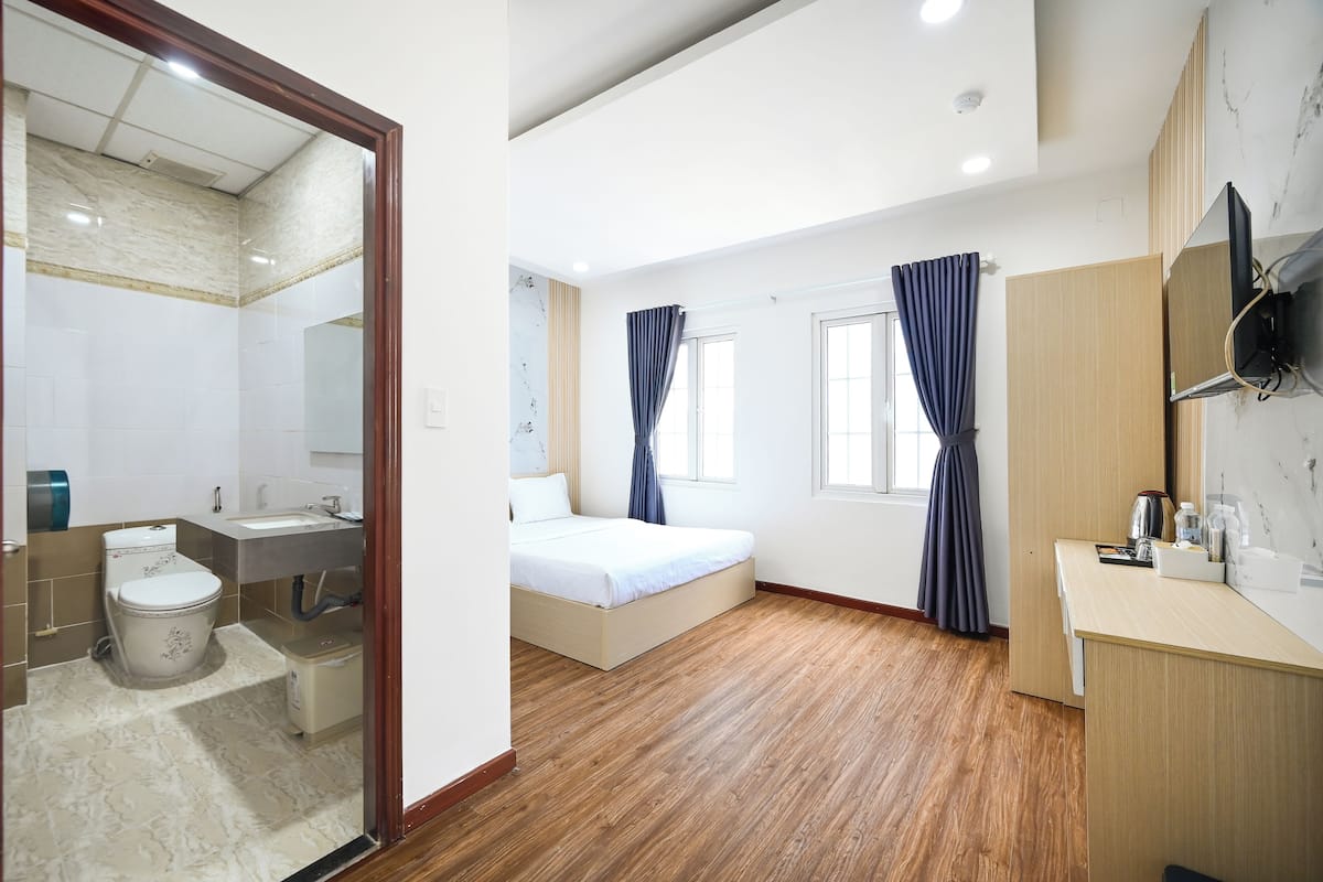 Une chambre d’hôtel avec un plancher en bois, un lit, un bureau, une télévision et une salle de bain équipée de toilettes et d’un lavabo.