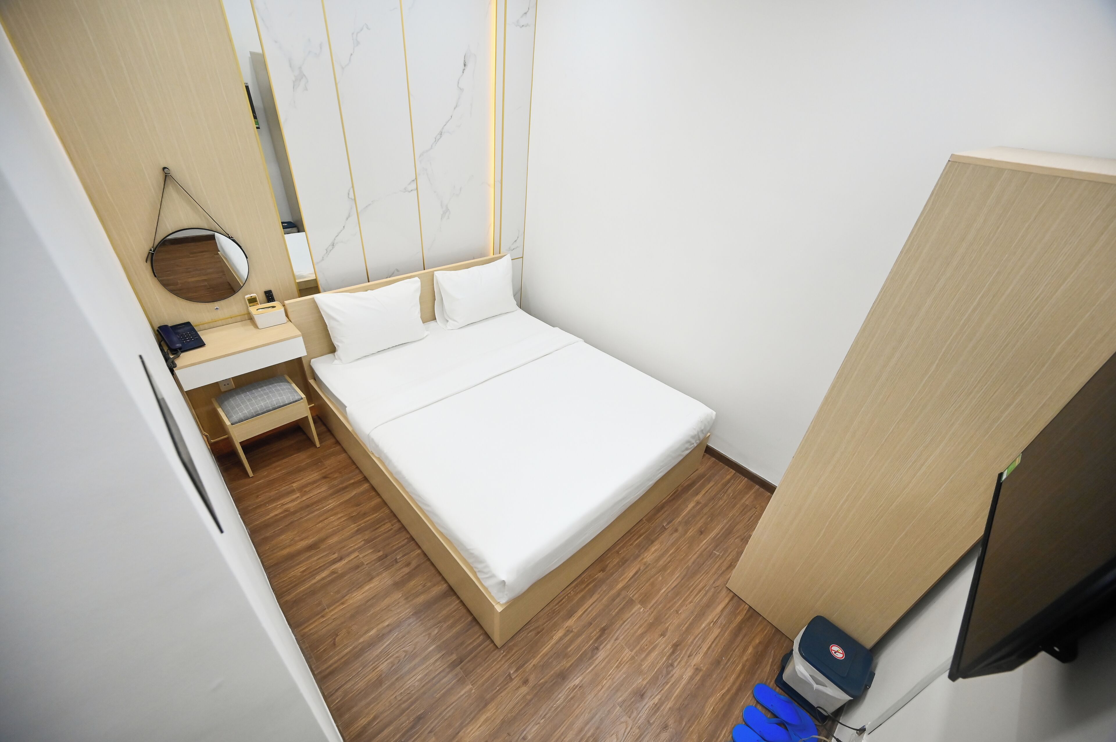 Een kleine, verzorgde slaapkamer met een enkel bed, een nachtkastje, een spiegel en een houten vloer.