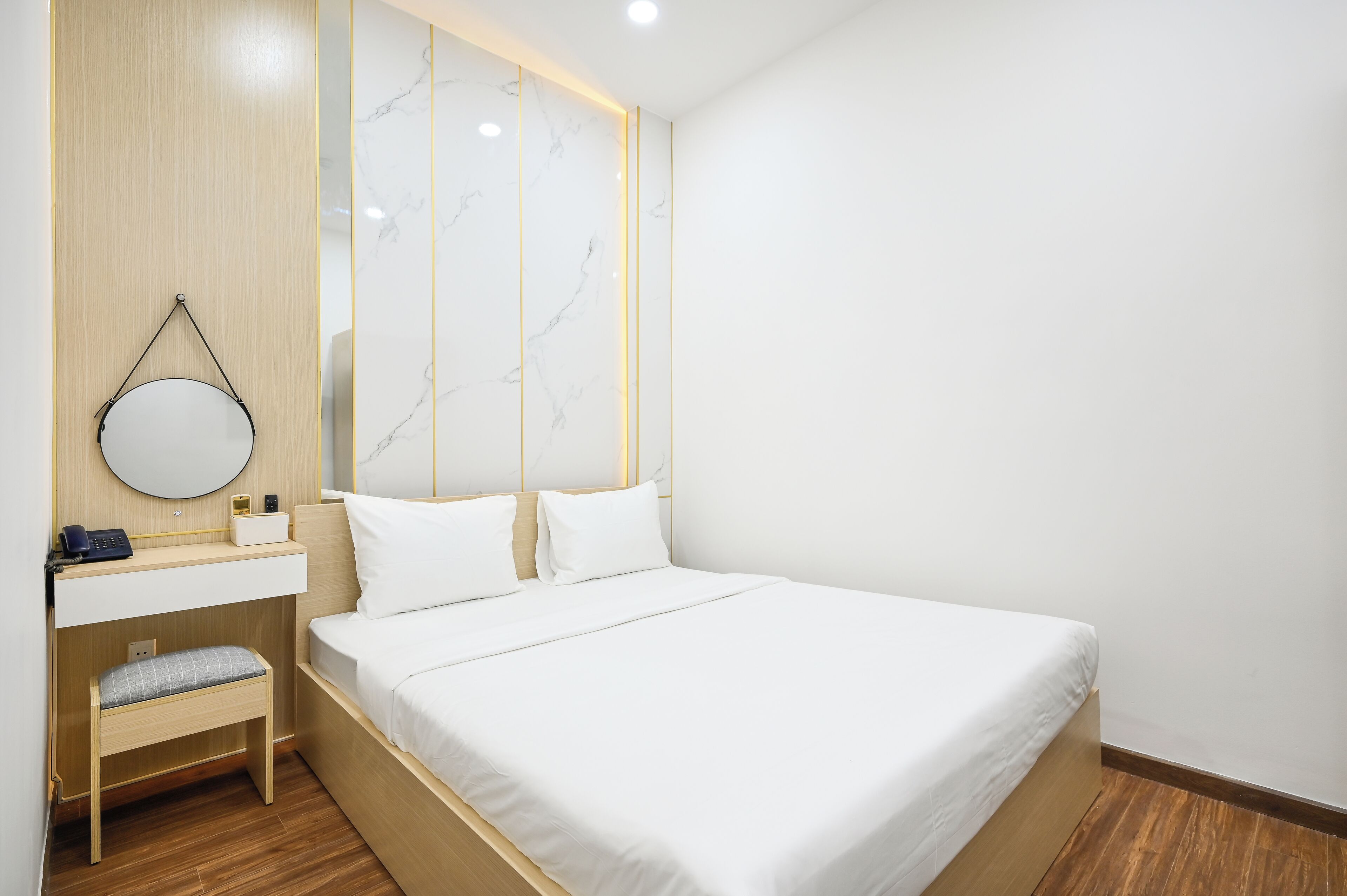 Una habitación de hotel moderna con una cama grande, una mesita de noche con espejo, un pequeño banco y un panel de pared de madera.