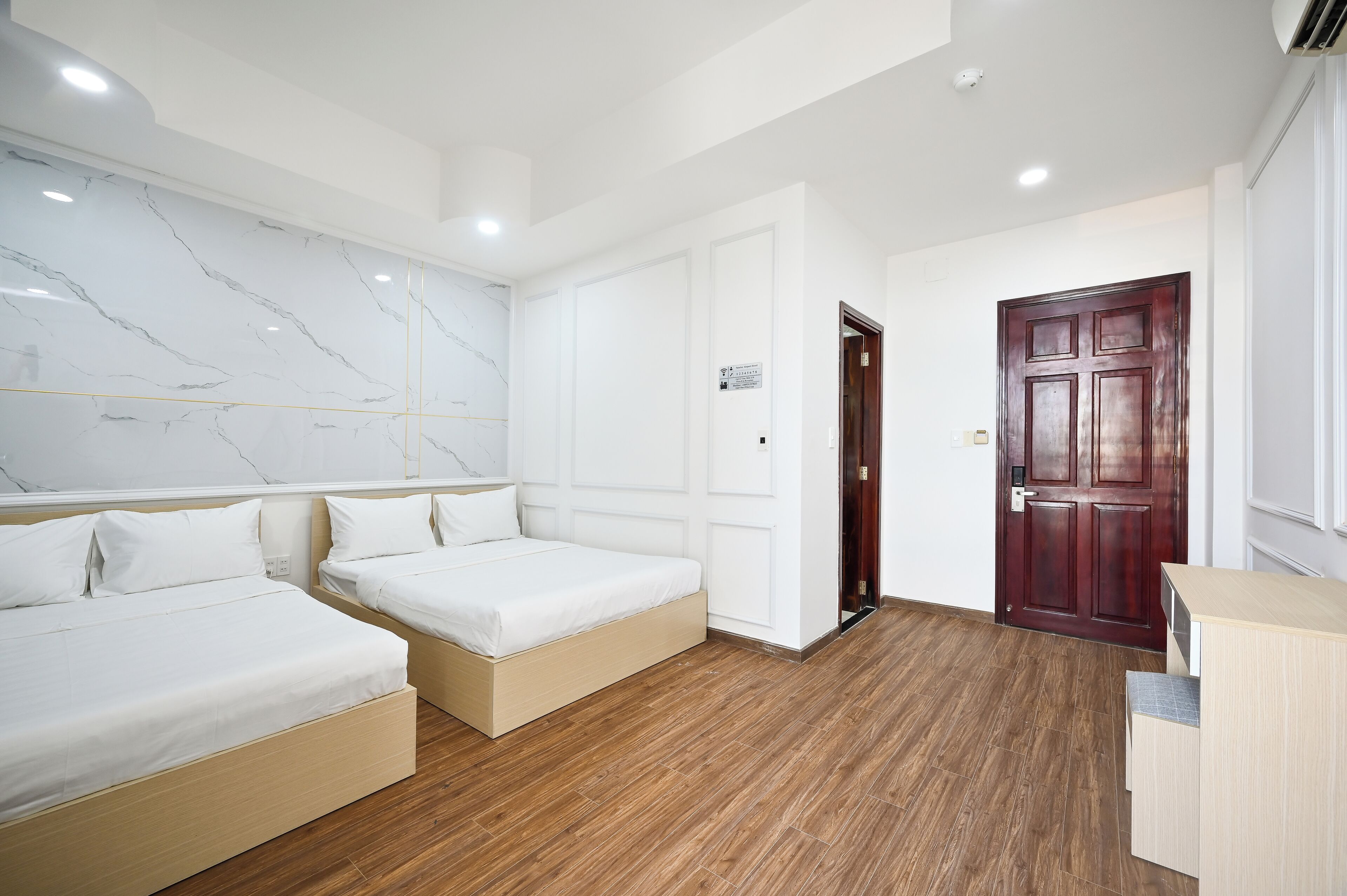 A modern hotel room with two beds, a marble wall, wooden flooring, and a dark wooden door.
