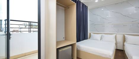 A modern hotel room with a bed, a small refrigerator, a wardrobe, and a balcony with a glass door.