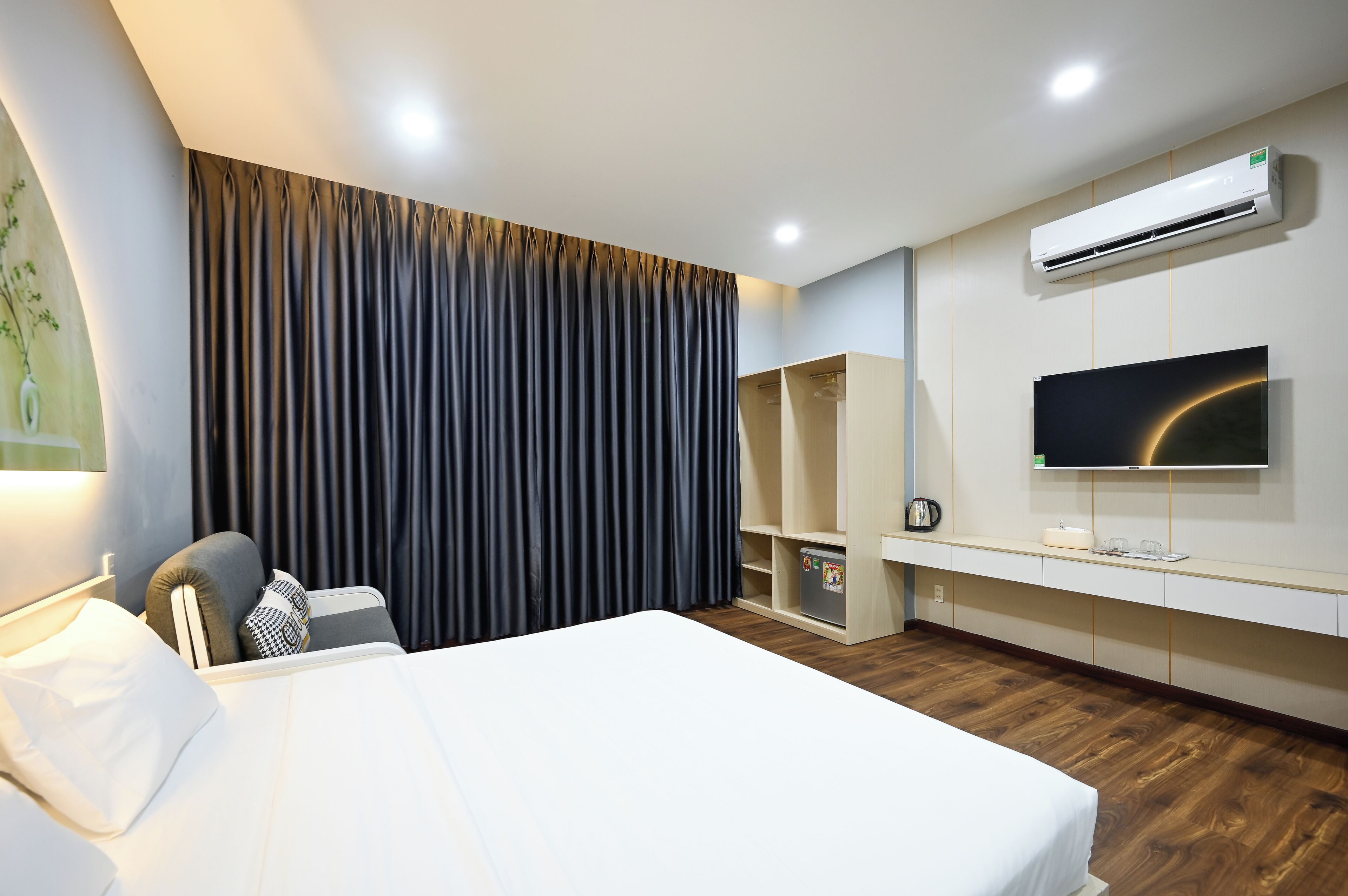 Habitación de hotel moderna con una cama grande, un televisor de pantalla plana, un armario y un equipo de aire acondicionado.