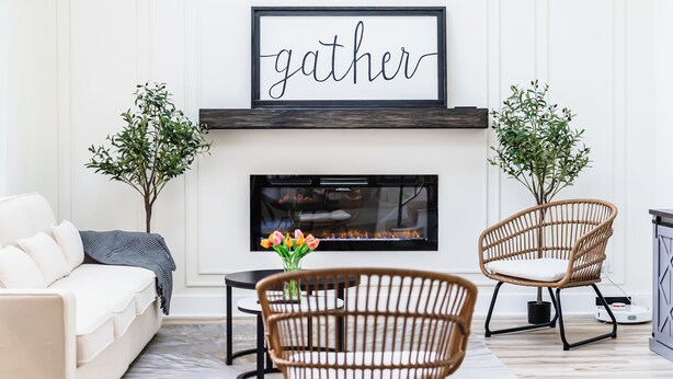 A living room with a fireplace, a sofa, two wicker chairs, a coffee table, and a framed sign above the fireplace that reads "gather". - Go Buckeyes!Stylish 3-Level Haven Near OSU,PS5,Skylight, Fully fenced Backyard (Columbus)