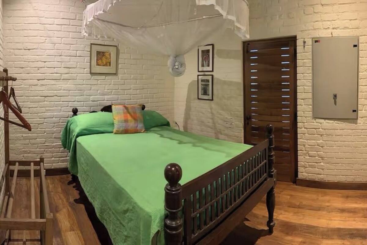 Una habitación con una cama y un armario de madera, pared de ladrillo blanco y techo blanco.