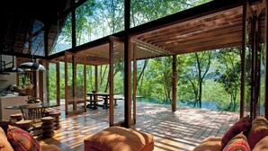 A spacious living area with a wooden deck, large windows, and a view of a forest. - Guava House by The Serendipity Collection (Hemmathagama)