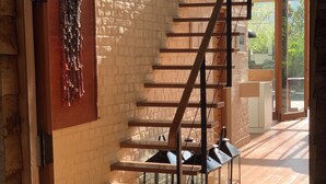 A staircase with wooden steps and metal railings, leading to a room with a brick wall and a hanging decorative piece. - Guava House by The Serendipity Collection (Hemmathagama)
